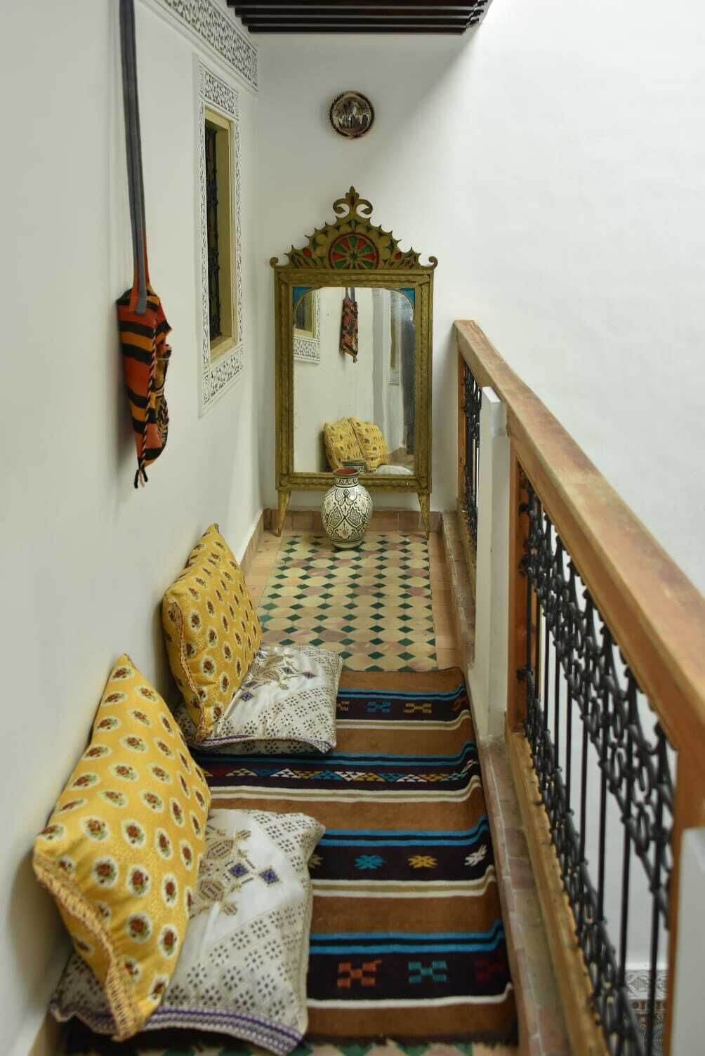 A narrow hallway with patterned rugs, a wooden railing, and a mirror with a decorative frame.