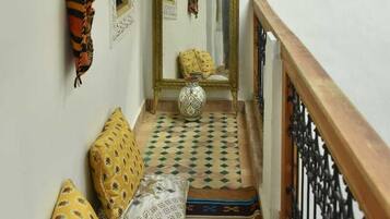 A narrow hallway with patterned rugs, a wooden railing, and a mirror with a decorative frame.