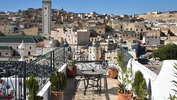 Una terraza con una mesa y sillas, plantas en macetas y vistas a un paisaje urbano con edificios y una torre.