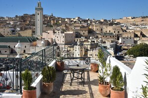 A terrace with a table and chairs, potted plants, and a view of a cityscape with buildings and a tower. - Riad Fes Elkaid (Fes)
