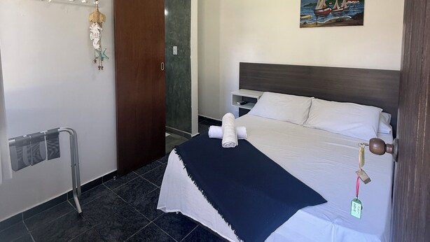A hotel room with a bed, a painting, a towel rack, and a door. - Pousada Bahan (Ubatuba)