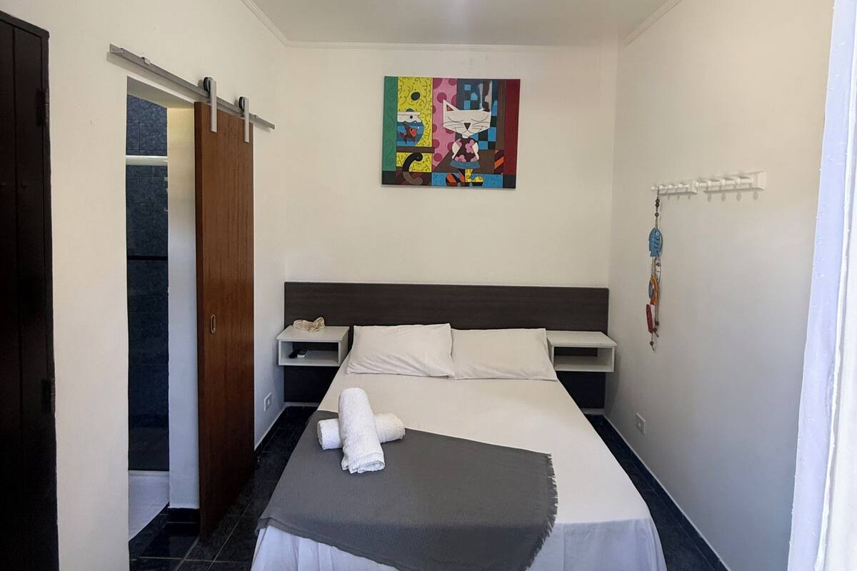 A hotel room with a bed, a painting, a bedside table, a nightstand, a wardrobe, and a door.