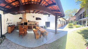 An outdoor patio with a brick fireplace, wooden furniture, and a tiled floor. - Pousada Bahan (Ubatuba)