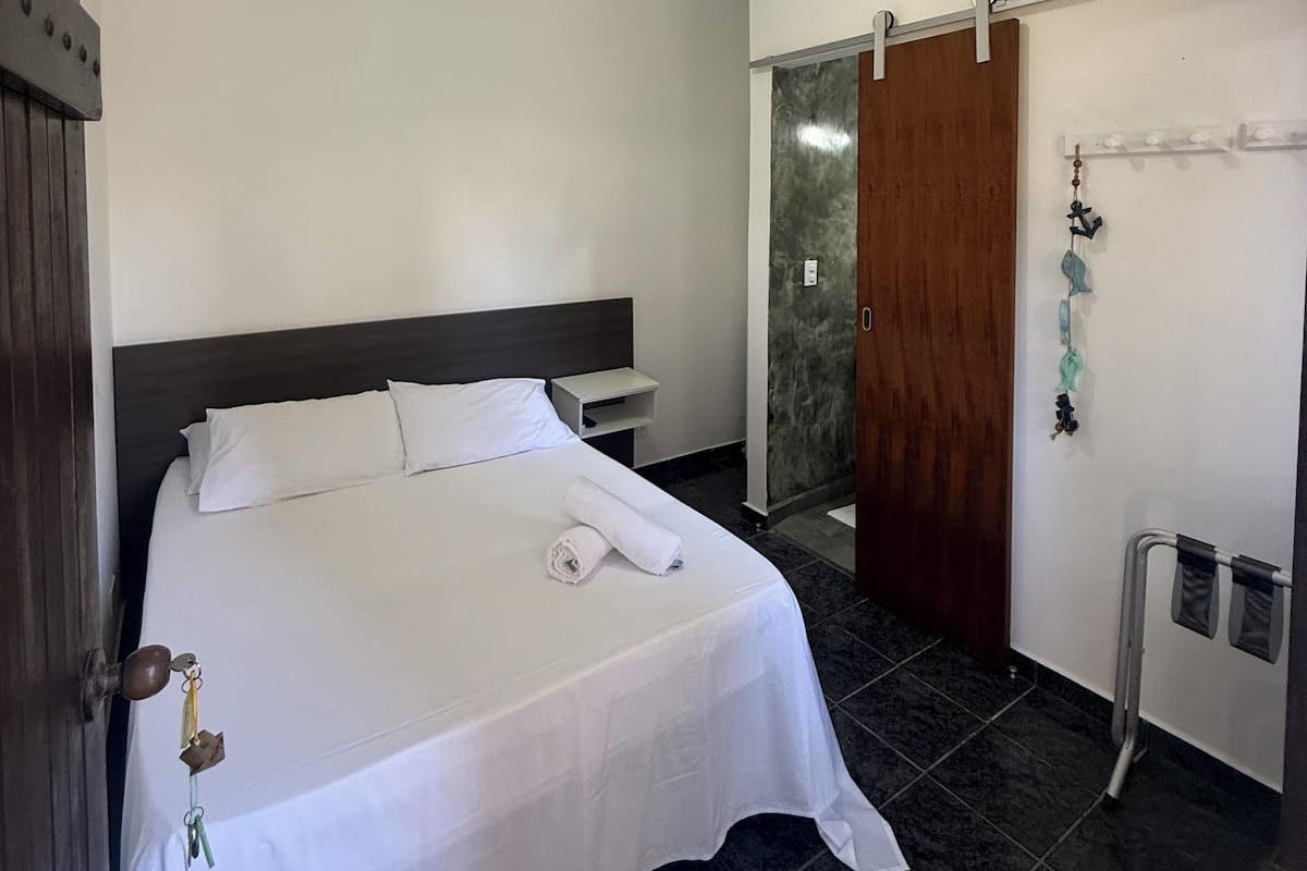 A hotel room with a bed, a TV mounted on the wall, a wooden door, and a small shelf with decorative items.