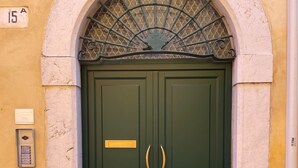 A double green door with a metal grille above it, set in a yellow wall with a number '15' sign above the door. - A view on Brescia's rooftops (Brescia)