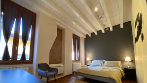 A bedroom with a bed, bedside lamps, a chair, a radiator, and a window with curtains. - A view on Brescia's rooftops (Brescia)