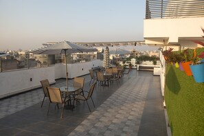 A rooftop terrace with tables and chairs, striped umbrellas, and a view of the cityscape. - Posh Residency (Gurugram)