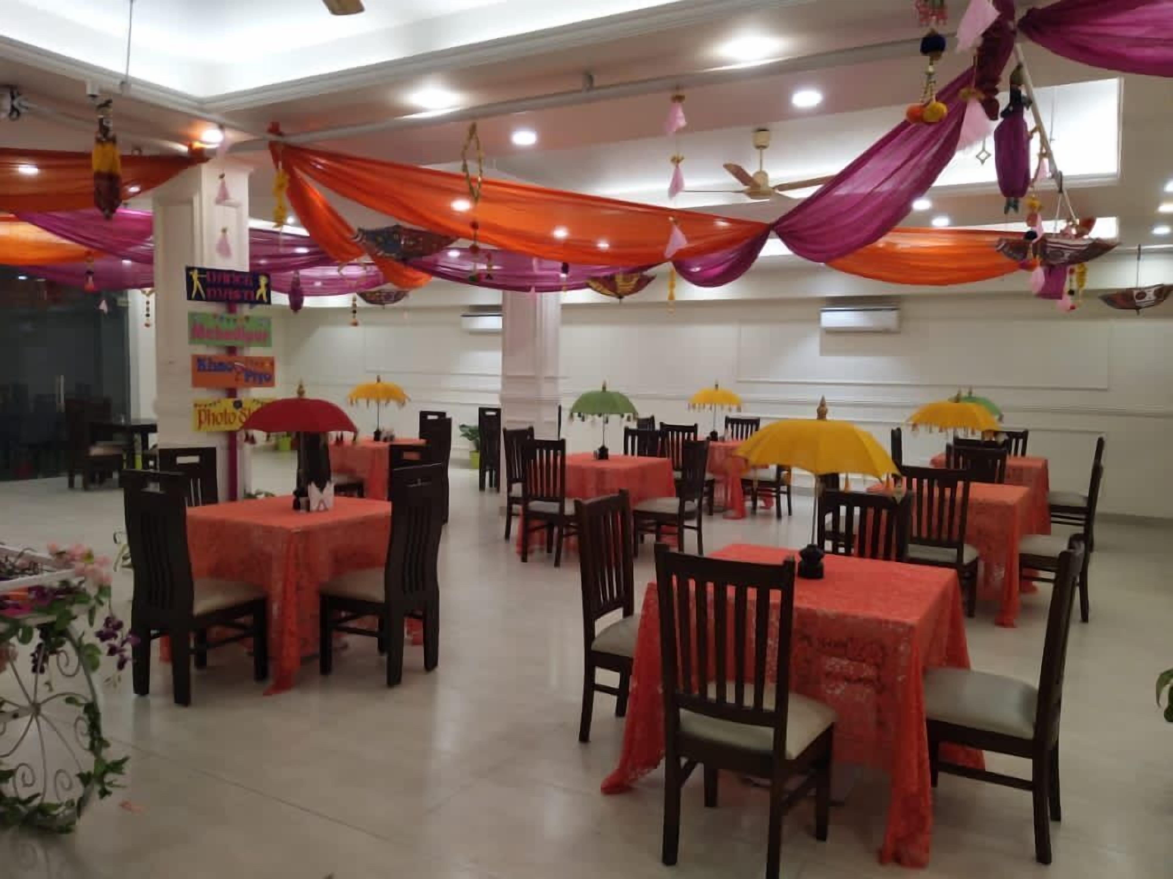 A banquet hall with tables covered in red tablecloths and chairs, decorated with hanging fabric and umbrellas.