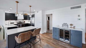 A modern kitchen with a central island, bar stools, and a wine refrigerator. - Magnificent Gulf View Condo 2 Bedroom Condo by RedAwning (Marco Island)