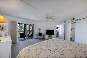 A hotel room with a bed, a desk, a television, a ceiling fan, and a sliding glass door leading to a balcony. - Magnificent Gulf View Condo 2 Bedroom Condo by RedAwning (Marco Island)