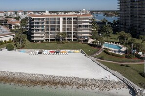 A beachfront hotel with a large sandy pool, multiple balconies, and a view of the ocean and other buildings. - Magnificent Gulf View Condo 2 Bedroom Condo by RedAwning (Marco Island)