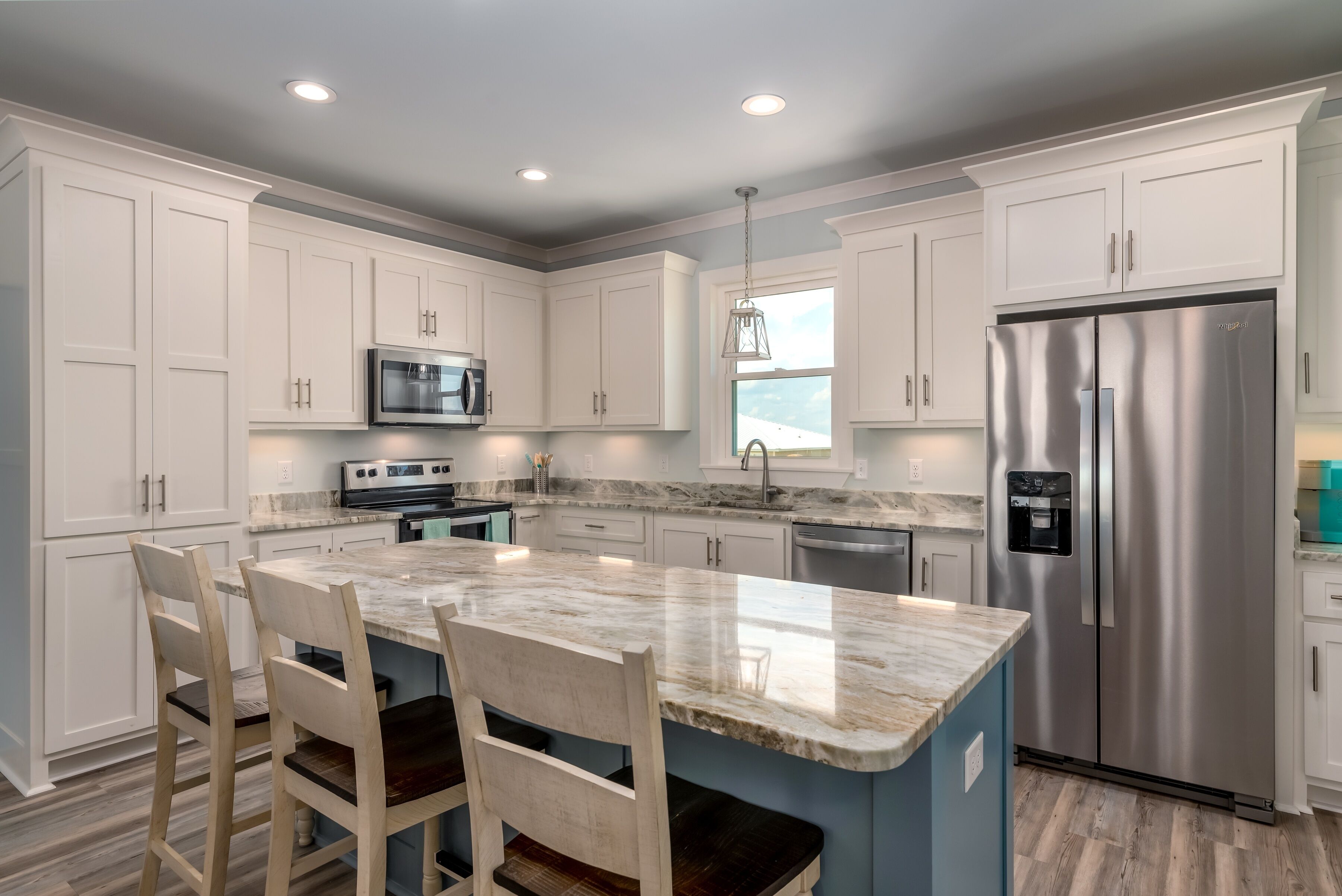A modern kitchen with white cabinets, a stainless steel refrigerator, a marble island, and a built-in microwave.