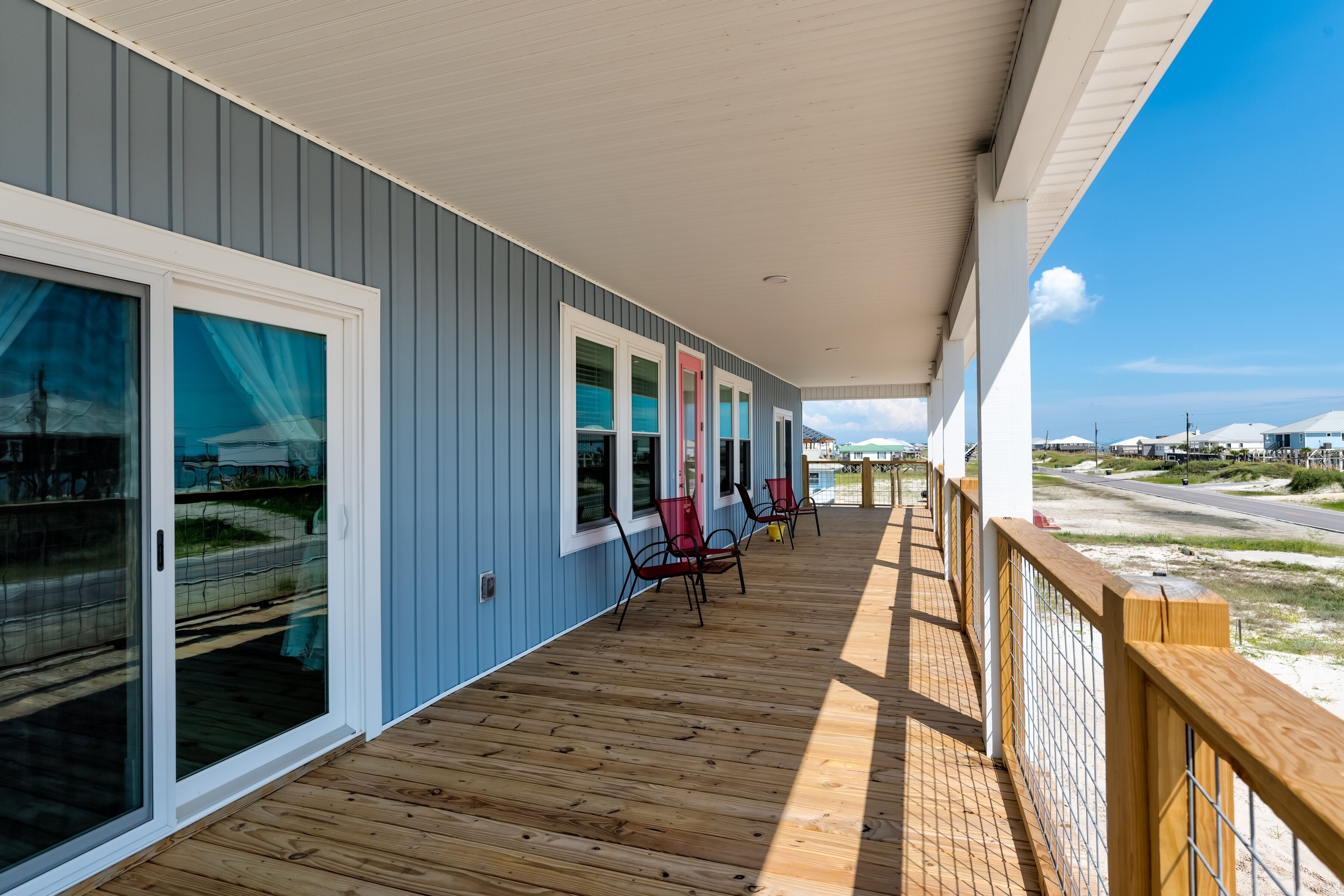 A covered outdoor area with a wooden deck, sliding glass doors, and red chairs.