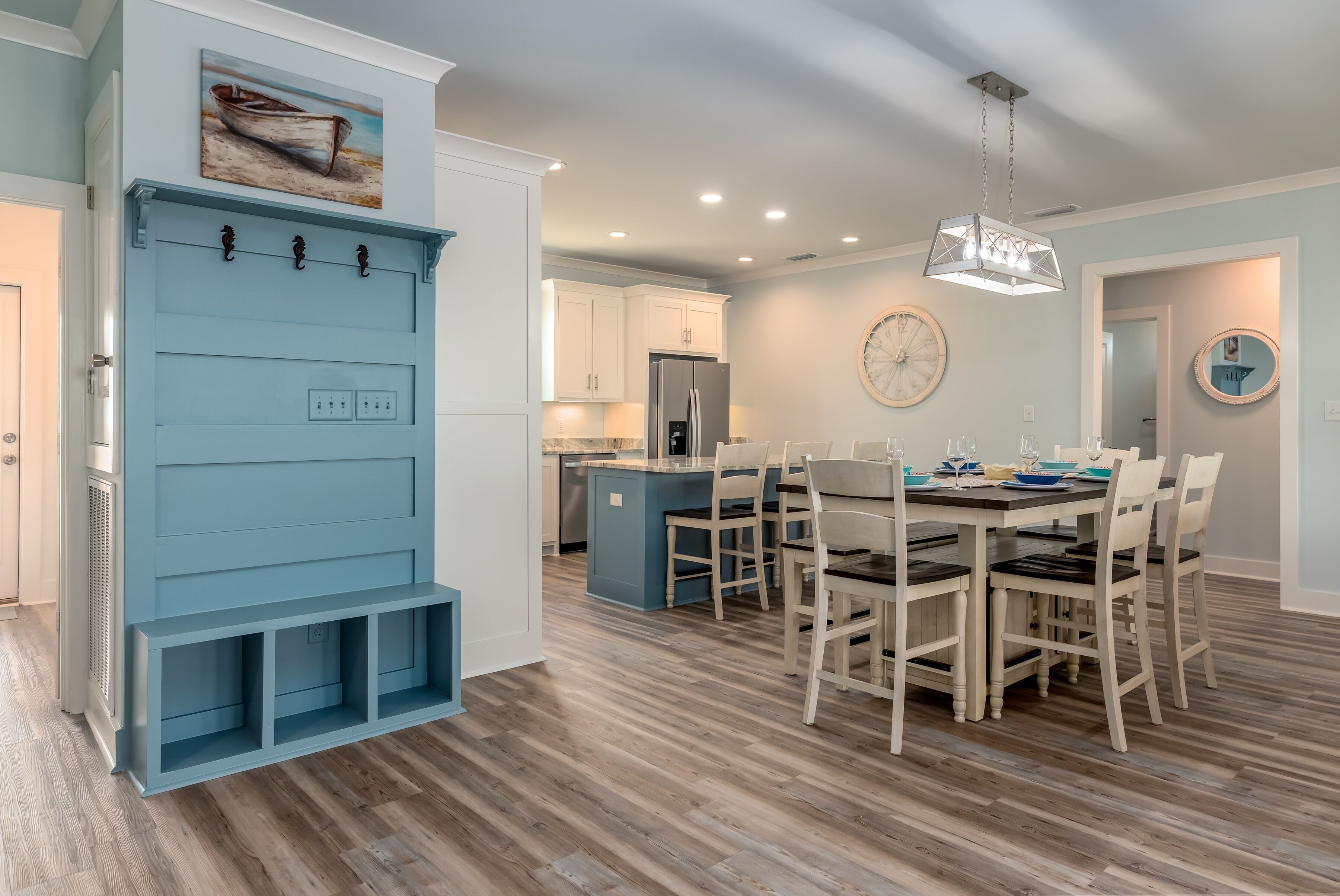 A modern kitchen with white cabinets, a blue island, and a dining area with wooden chairs.
