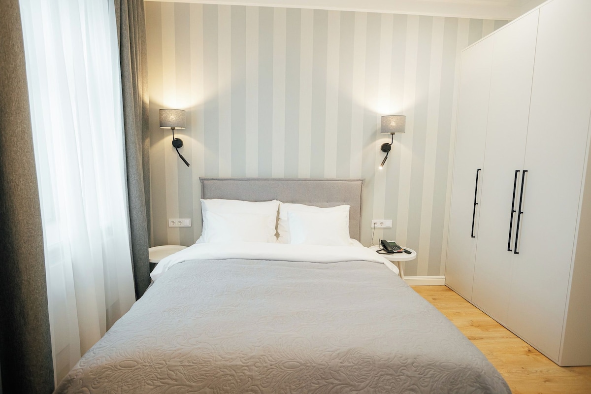 A neatly arranged bedroom with a bed, bedside lamps, a nightstand, and a wardrobe.