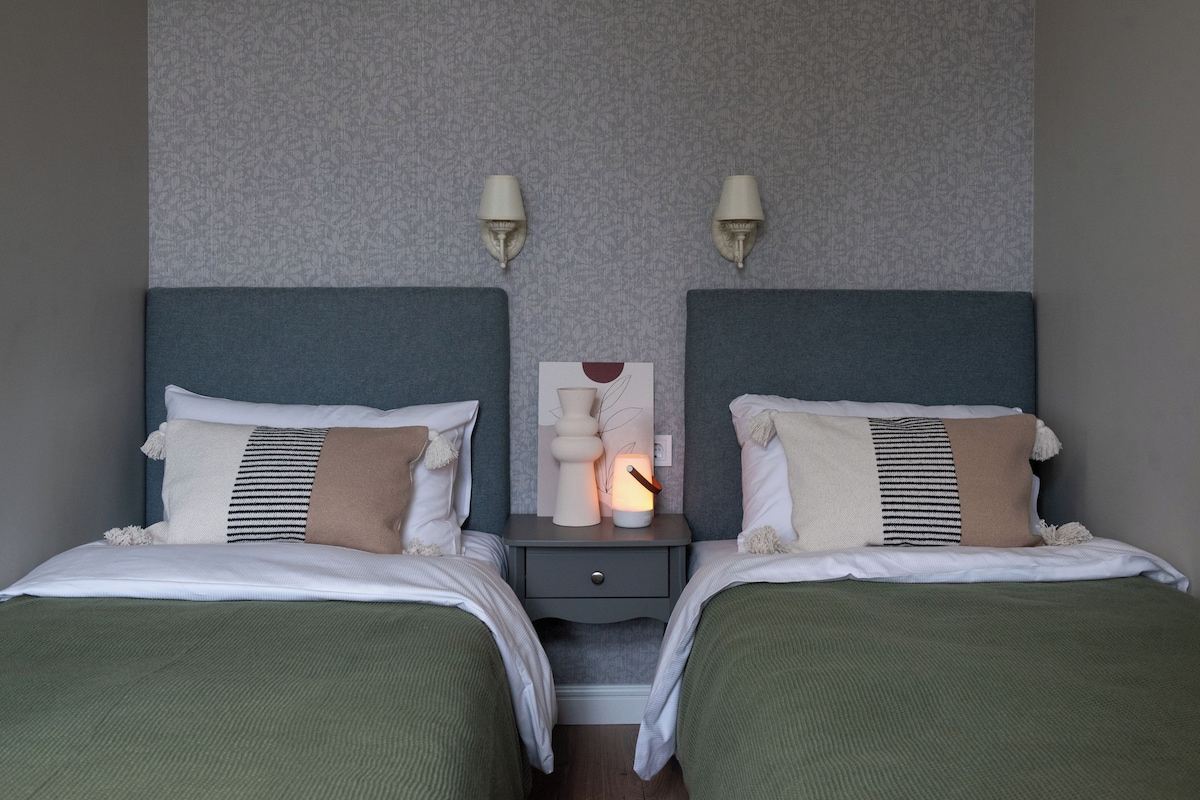 A hotel room with two beds, a nightstand with a lamp, and a wall-mounted artwork.