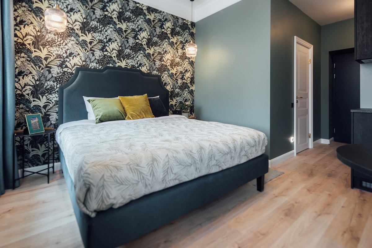 A bedroom with a large bed, a dark headboard, and a floral wallpaper.