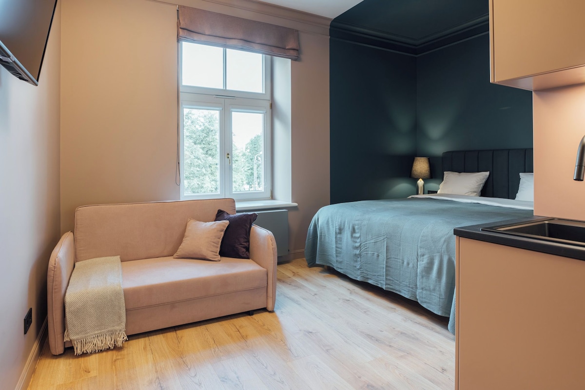 A modern bedroom with a bed, a sofa, a window, and a bedside table.