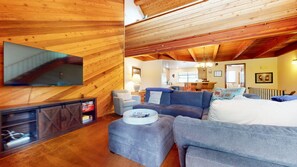 Una sala de estar acogedora con televisor, sofás, una mesa de centro y una cocina al fondo.