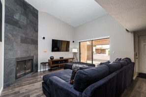 Una sala de estar moderna con una pared de piedra, un televisor de pantalla plana, una chimenea, un sofá y un gran ventanal corredizo que da a un espacio exterior.