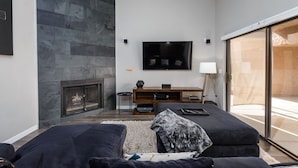 Un salon moderne avec un mur en pierre, une cheminée, un téléviseur à écran plat et une grande fenêtre.
