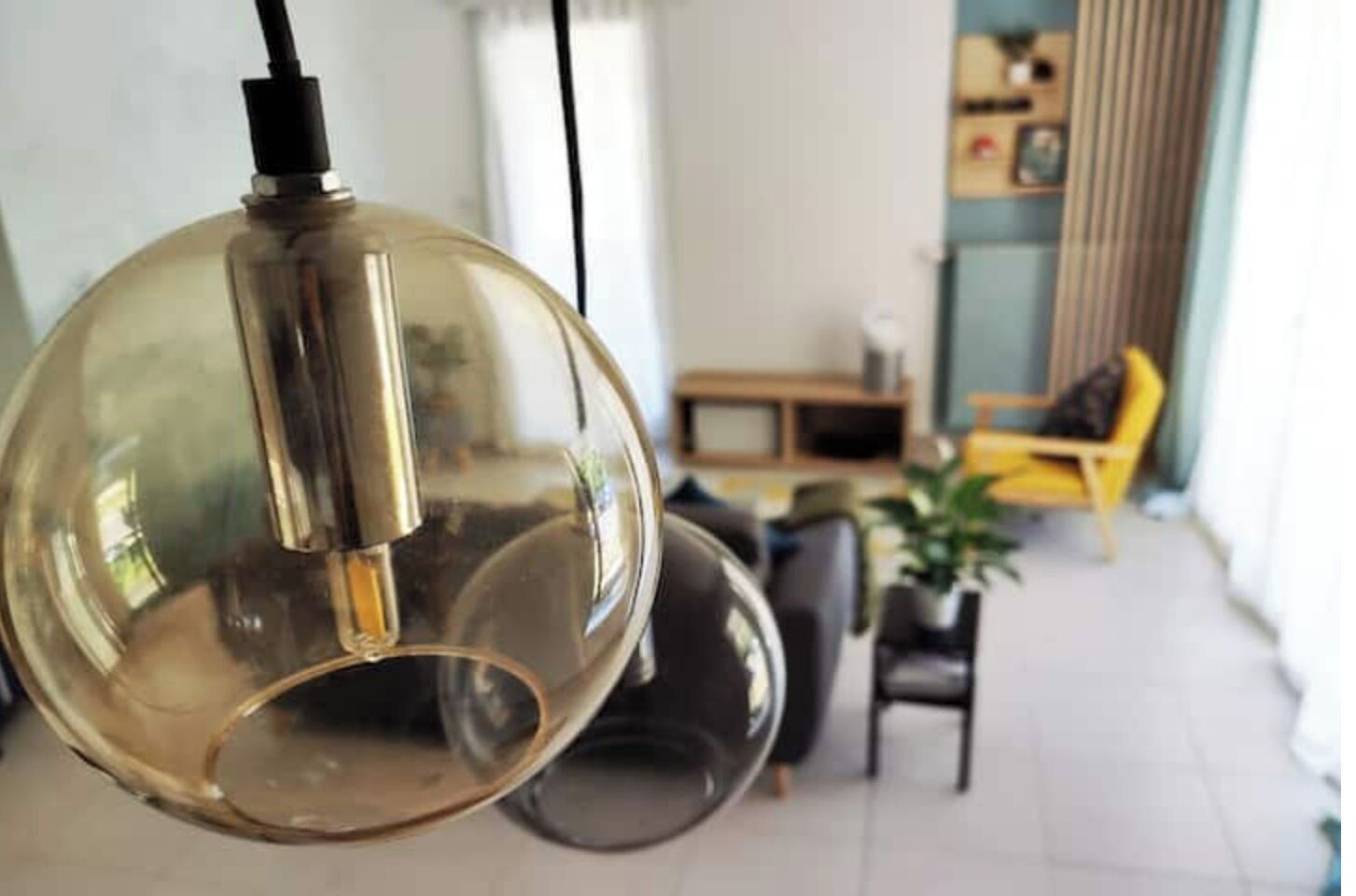Een bolvormige hanglamp in een woonkamer met een modern design, een gele stoel en een plant op de achtergrond.