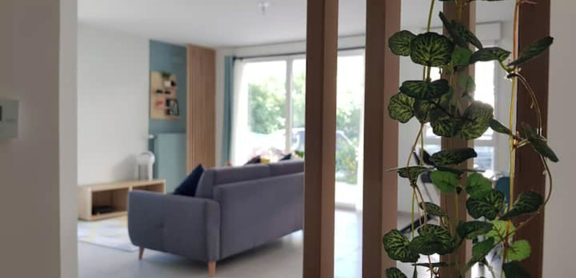 A modern living room with a grey sofa, a wooden bench, and a large window.