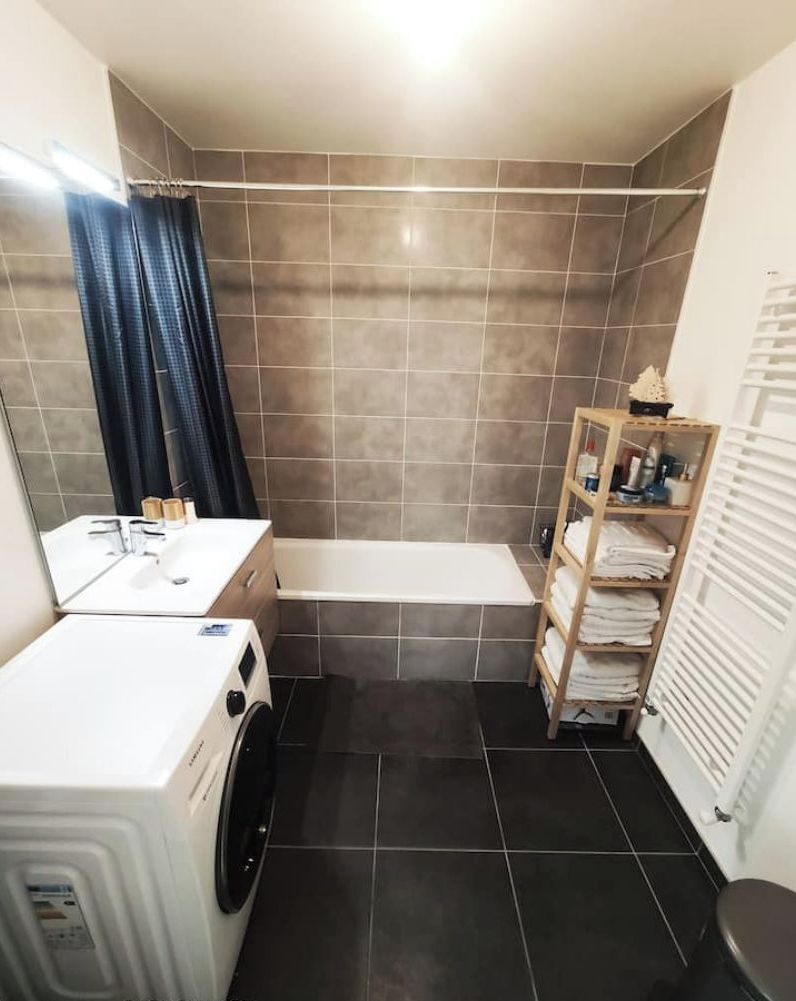 A compact bathroom with a white sink, a bathtub, and a laundry machine.