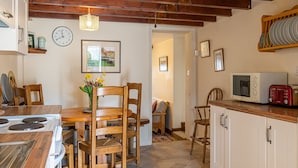 A kitchen with wooden chairs, a dining table, a stove, a microwave, and a clock on the wall. - High Wallabarrow Farm Cottage -  Duddon Valley (Ulpha)