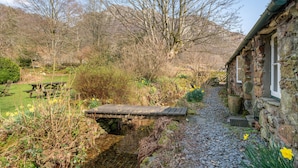 A stone building with a stone pathway leading to a wooden bridge over a stream. - High Wallabarrow Farm Cottage -  Duddon Valley (Ulpha)
