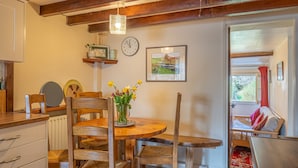A cozy room with a wooden dining table, chairs, a clock, a framed picture, and a window with a view of greenery. - High Wallabarrow Farm Cottage -  Duddon Valley (Ulpha)