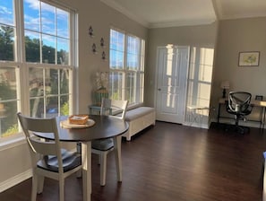 A spacious room with a dining table and chairs, a bench, a door, and a small desk with a chair. - Boston Area, Beautiful Sunsets & Free Parking (Braintree)