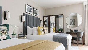Quarto de hotel moderno com duas camas, uma escrivaninha, uma cadeira, um espelho redondo e uma janela grande.