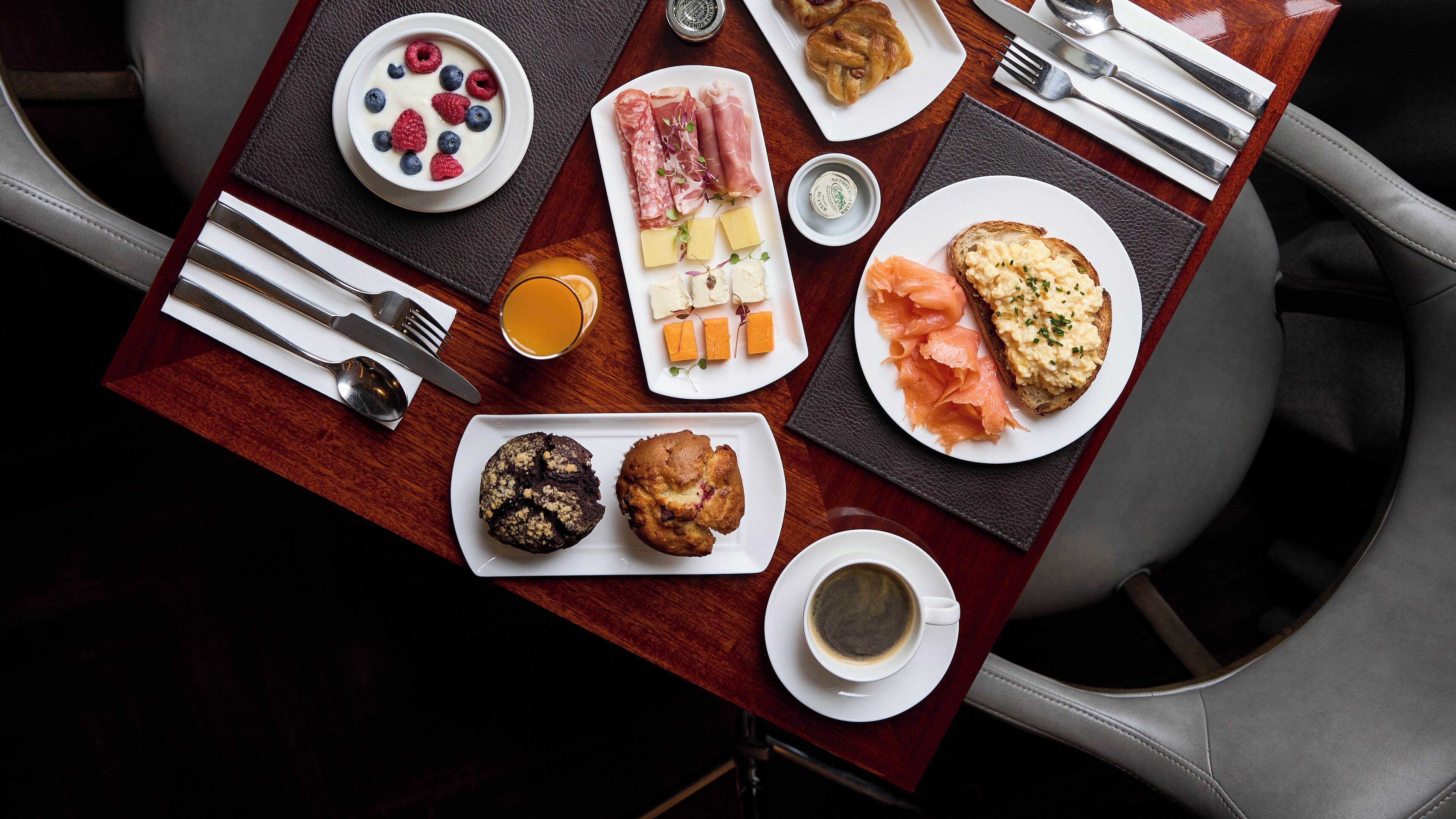 Une table dressée pour le petit-déjeuner, avec divers aliments, des ustensiles et une tasse de café.