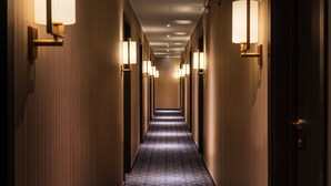 A hotel hallway with a carpeted floor, wall-mounted lamps, and doors on both sides. - The Selwyn Hotel (Richmond)