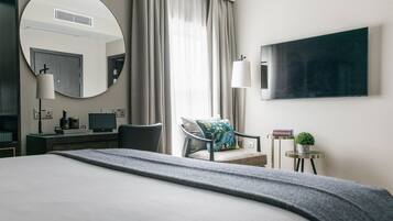 Une chambre d’hôtel moderne dotée d’un grand lit, d’un bureau avec un ordinateur, d’une chaise, d’un miroir rond, d’un téléviseur à écran plat et d’une petite table d’appoint avec une plante.
