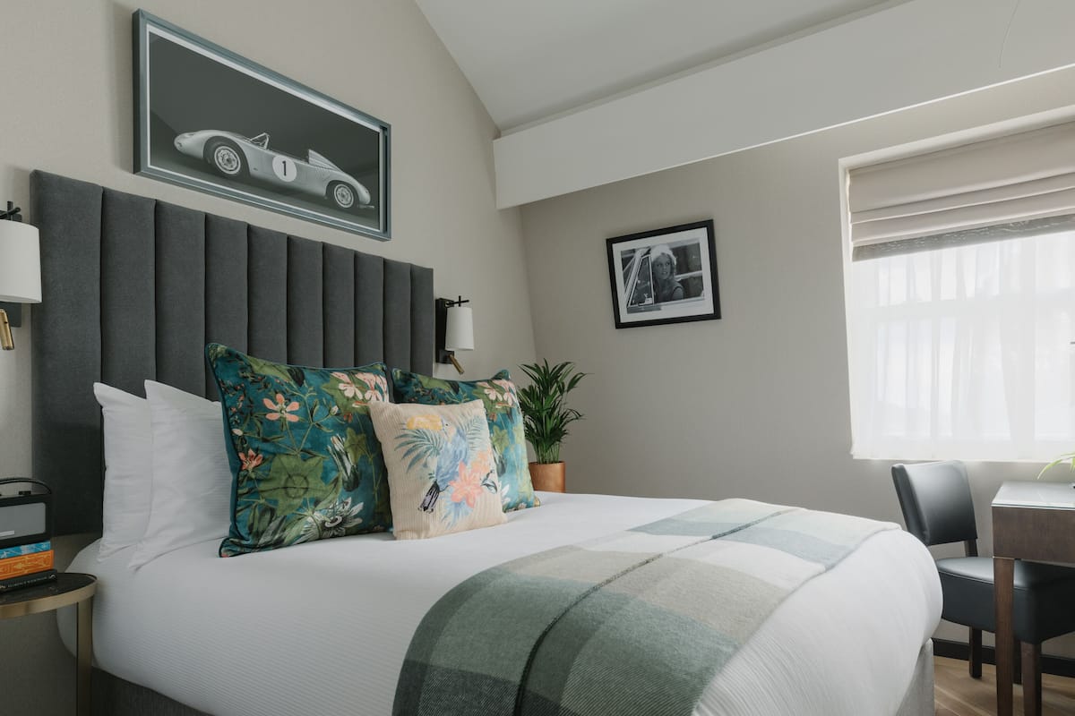 A modern bedroom with a large bed, a headboard, a desk with a chair, a potted plant, and a framed picture on the wall.