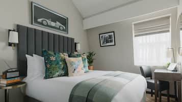 Um quarto moderno com uma cama grande, cabeceira, escrivaninha com cadeira, planta em vaso e um quadro na parede.