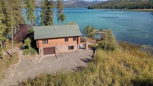 Una baita con tetto verde, vialetto in pietra e vista su un lago circondato da alberi e colline.
