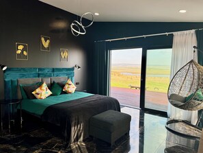 A modern bedroom with a large bed, a hanging chair, and a view of the countryside. - Luxurious smart villa in Golden Circle, Reykholt, South Iceland (Reykholt)