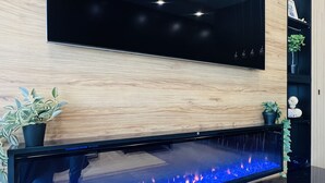 Un salon moderne avec un téléviseur à écran plat fixé à un mur en bois, un aquarium intégré avec un éclairage bleu, et un meuble de rangement noir agrémenté d’objets décoratifs.