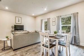 A living room with a sofa, TV, and dining table with chairs. - Elegant townhome + oversized luxury pool (Pensacola)
