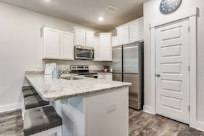 A modern kitchen with white cabinets, a stainless steel refrigerator, a microwave, and a granite countertop. - Elegant townhome + oversized luxury pool (Pensacola)