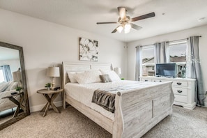 A bedroom with a bed, bedside tables, a ceiling fan, a TV, and a window with curtains. - Elegant townhome + oversized luxury pool (Pensacola)