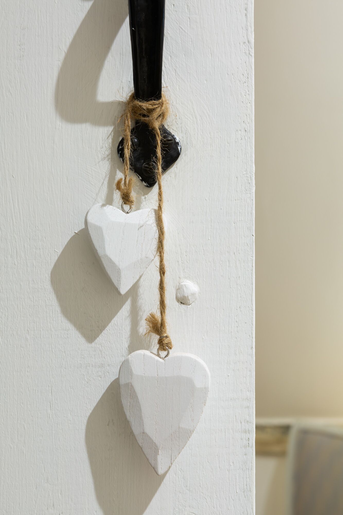 Un mur blanc orné d’un objet noir et de deux décorations en forme de cœur qui y sont suspendues.