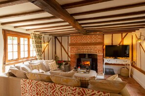 A cozy living room with a brick fireplace, wooden beams, a sofa set, and a television.
