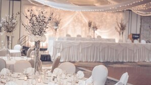 A banquet hall with round tables set for a formal event, draped with white fabric and illuminated by string lights. - Valhalla Hotel and Conference Centre (Thunder Bay)