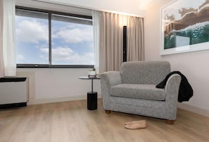 Una habitación con ventana, un sofá gris, una mesita con una planta y un cuadro en la pared.