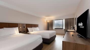 Habitación de hotel con dos camas, televisor, escritorio y ventana con vistas.