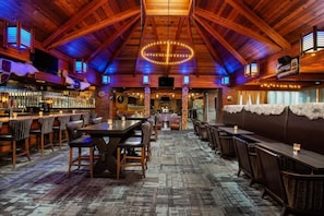 Un intĂ©rieur rustique avec des poutres en bois, un coin bar et diffĂ©rents espaces pour sâasseoir.